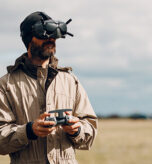 man flying a drone in a field with goggles on