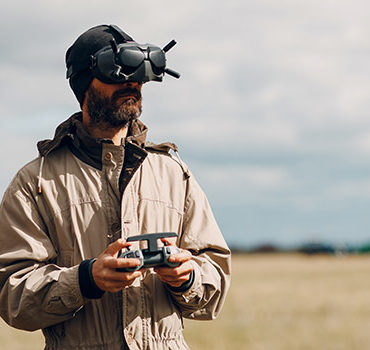 man flying a drone in a field with goggles on